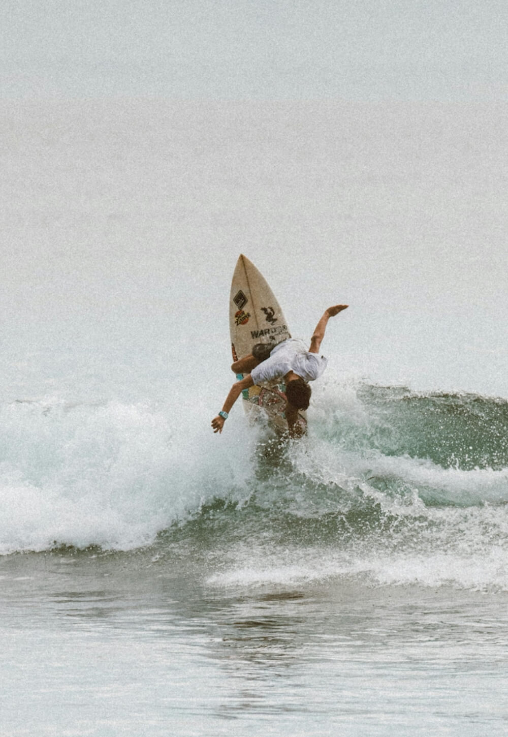 Surfer performing a maneuver on a wave with a branded surfboard in the ocean