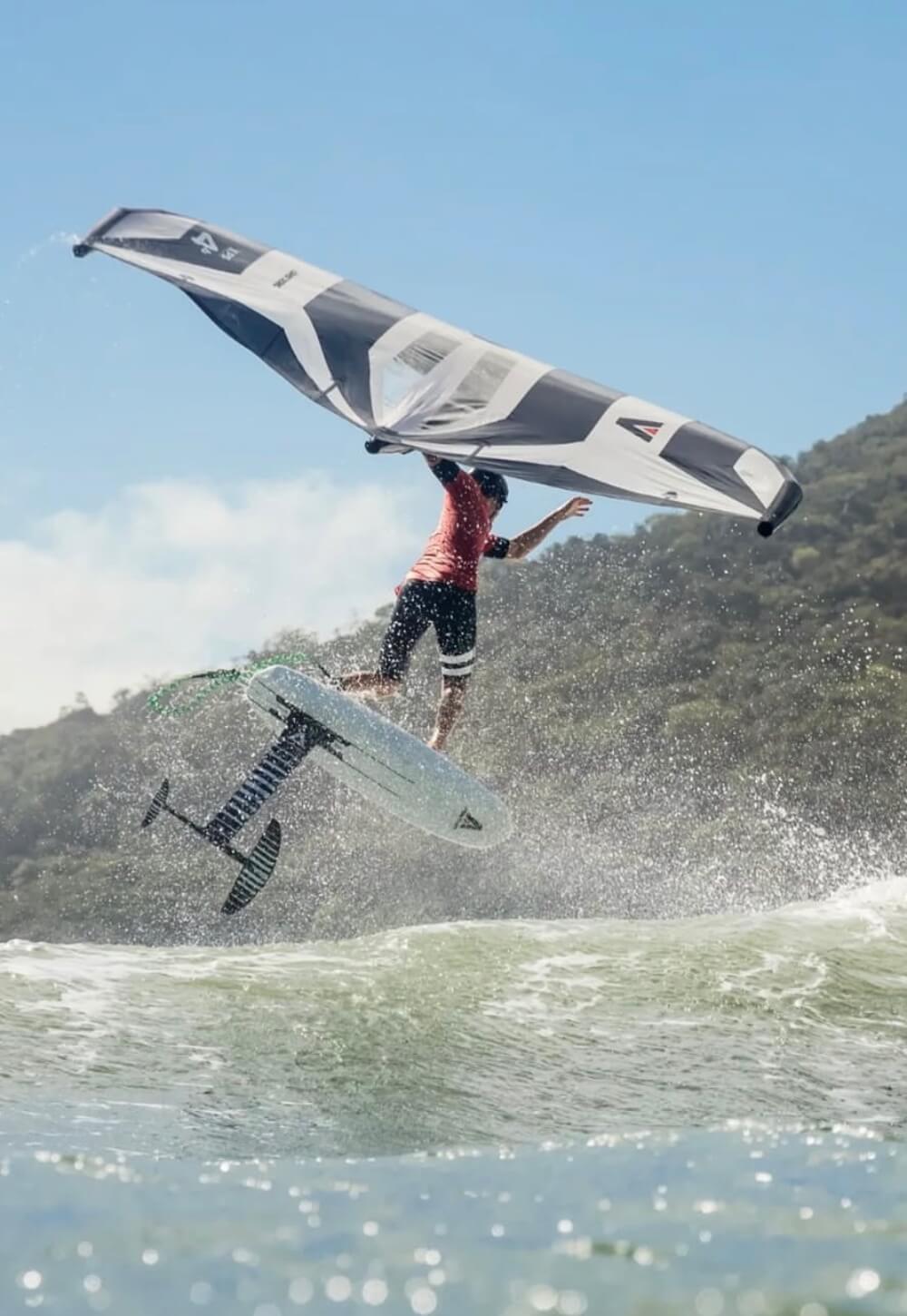 Athlete wingfoiling above ocean waves with foil board and sail, mid-air action shot