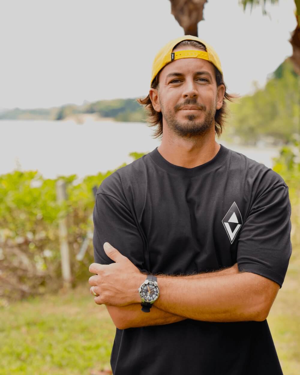 Portrait of the Salty brand founder standing outdoors in a black Salty logo t-shirt and yellow cap, arms crossed